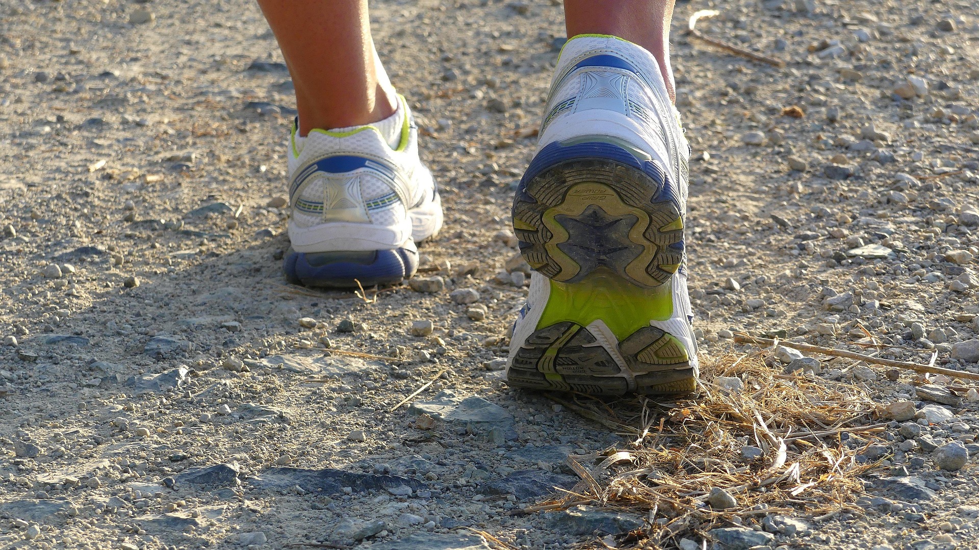 Close-up of running shoes walking on a gravel trail, representing physical activity